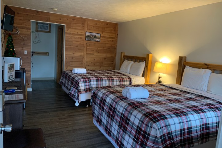 Cozy hotel room with two plaid-clad beds, a small lit lamp, and a mini fridge on a wooden floor.